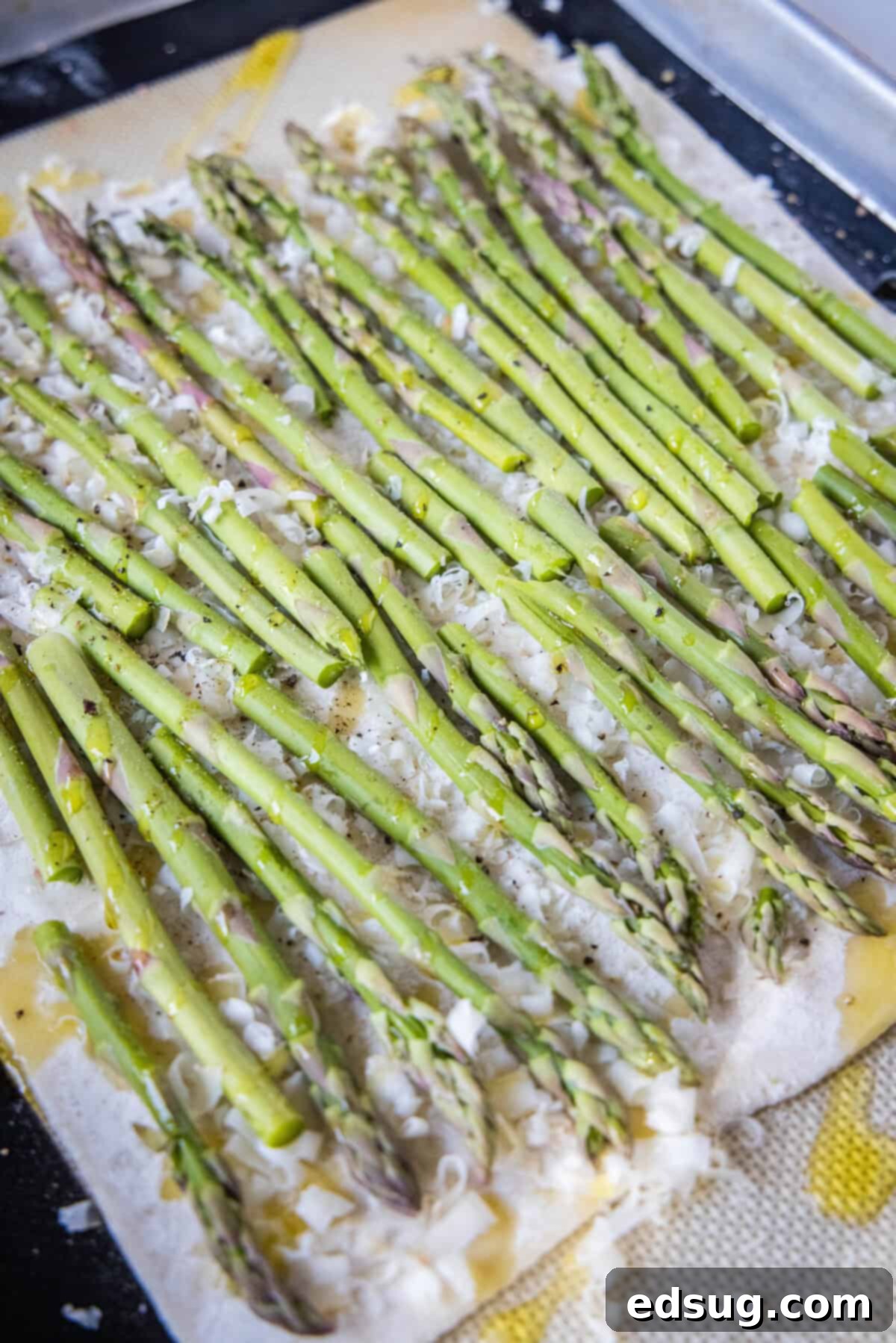 asparagus tart being assembled on a baking tray with cheese and asparagus arranged