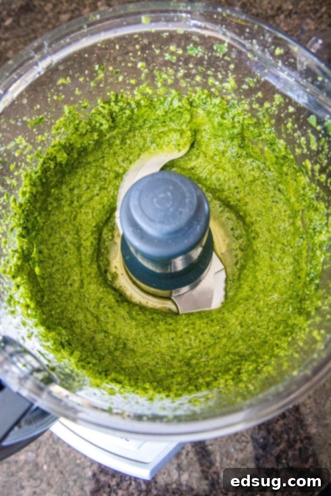 Overhead view of perfectly blended spinach pesto in a food processor bowl, showcasing its vibrant green color and smooth, rich texture.