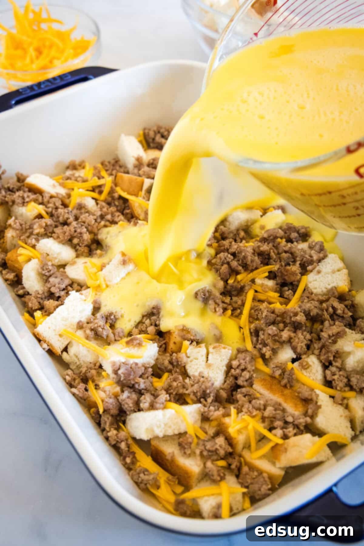 Egg mixture being poured over breakfast casserole ingredients in a baking dish.