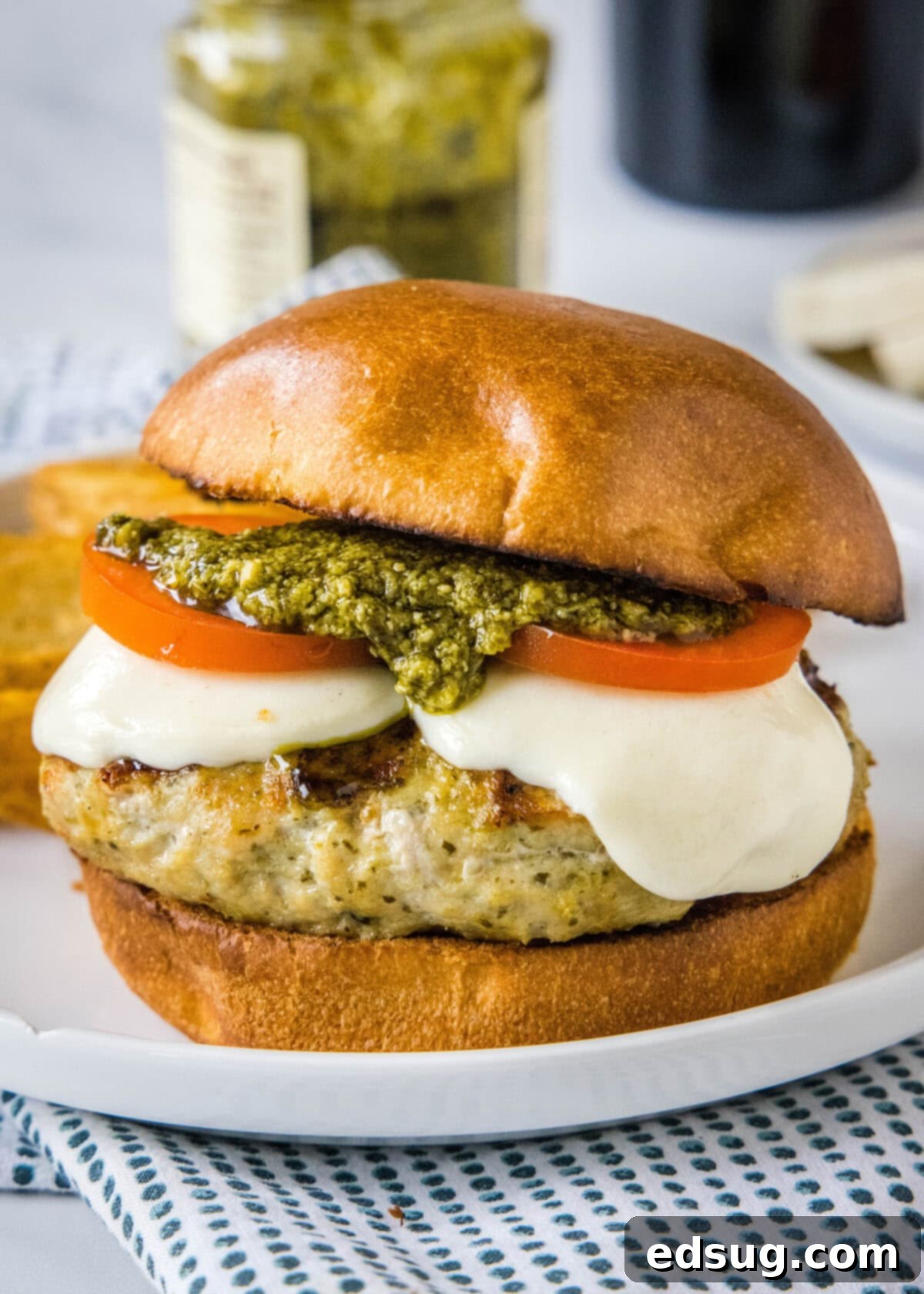pesto chicken burger on a plate, garnished with tomatoes and mozzarella