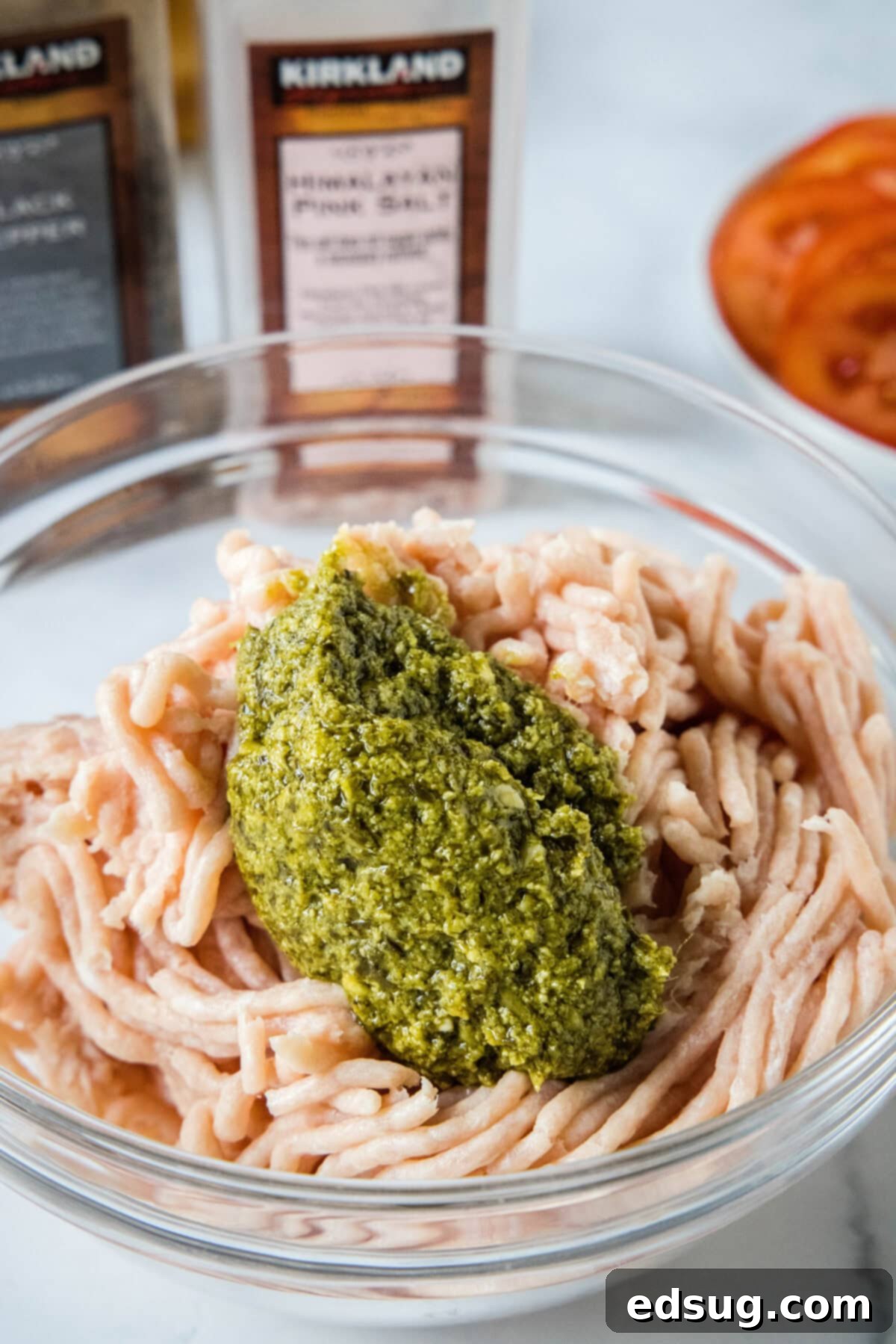 pesto being added to ground chicken in a mixing bowl