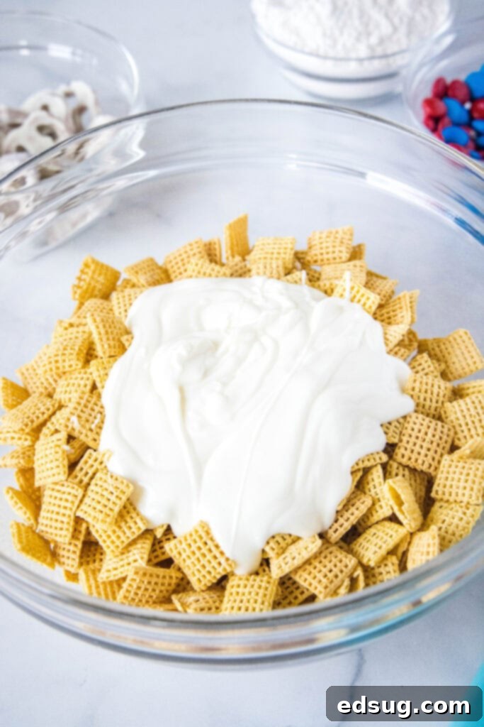 Pouring melted white chocolate over Chex cereal in a large mixing bowl, the initial step to creating Red, White & Blue Muddy Buddies.