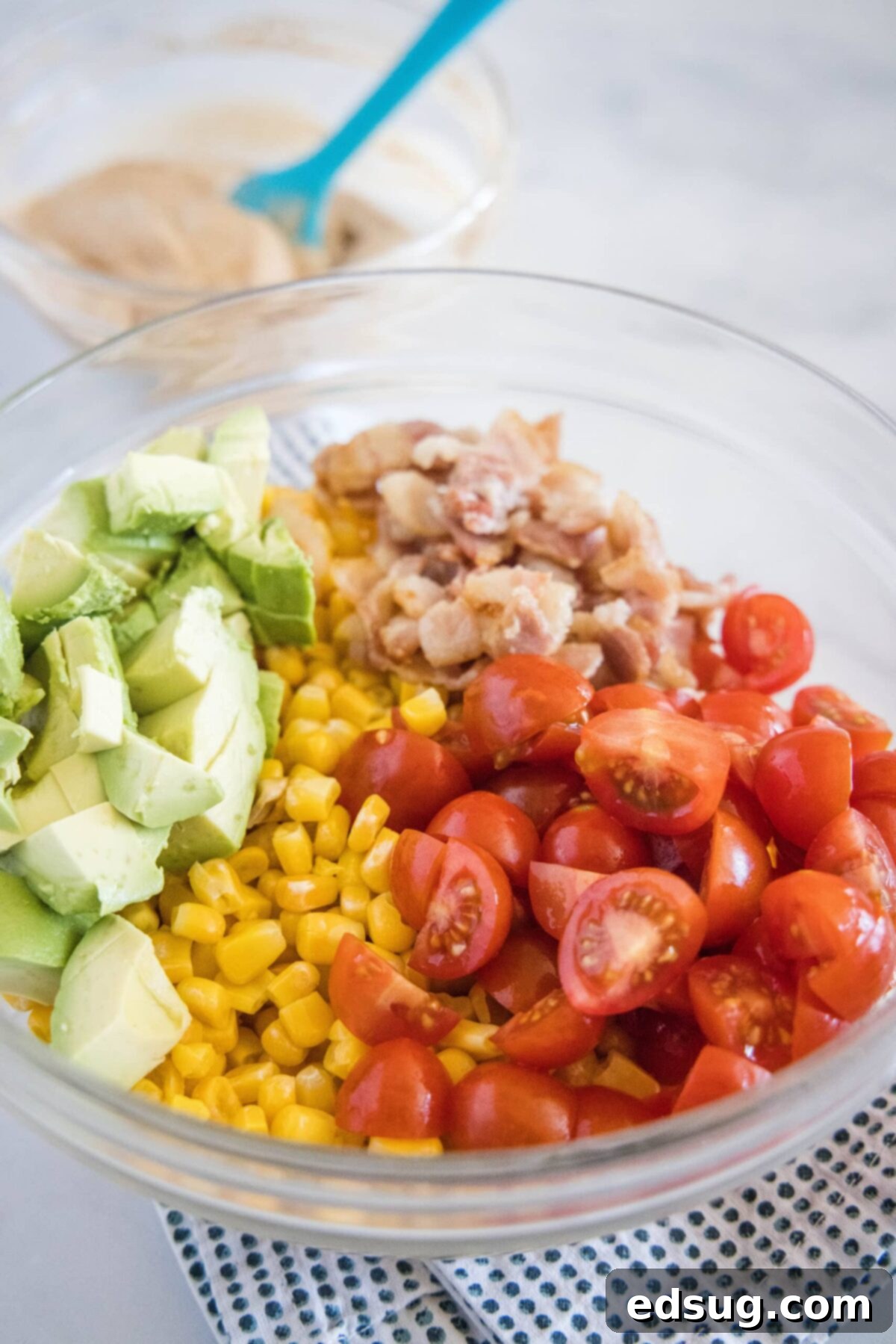 A mixing bowl with quartered cherry tomatoes, corn, pieces of bacon, and avocado
