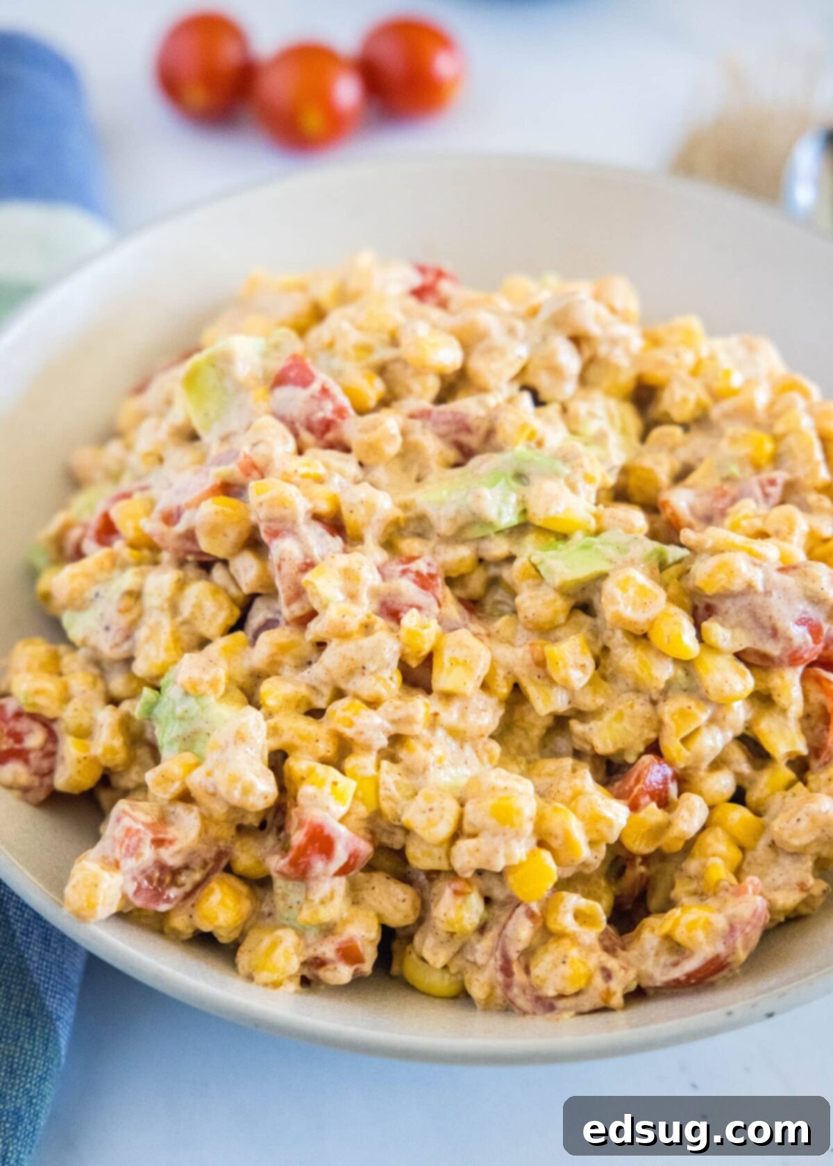 Close up of a bowl of corn salad with cherry tomatoes in the background