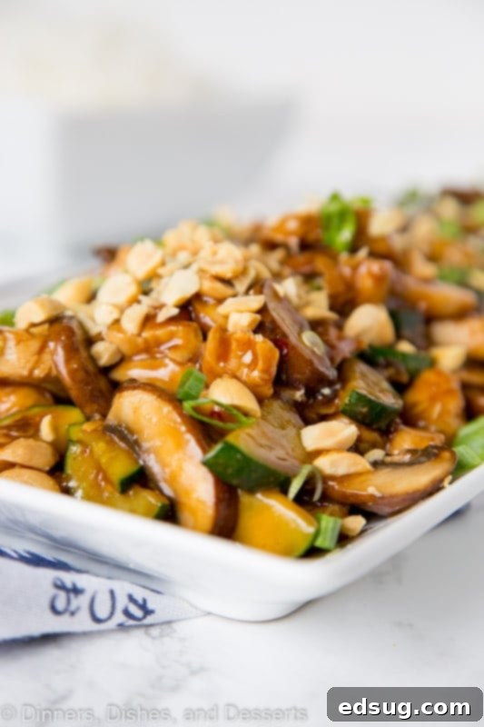 Close up view of glossy Kung Pao Chicken with peanuts and green onions on a white plate, ready to serve.