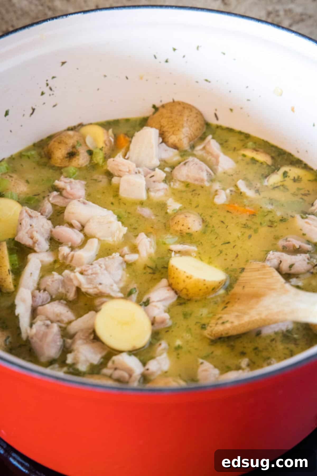 Browned chicken and potatoes being added to the sautéed vegetables and broth in a large pot.