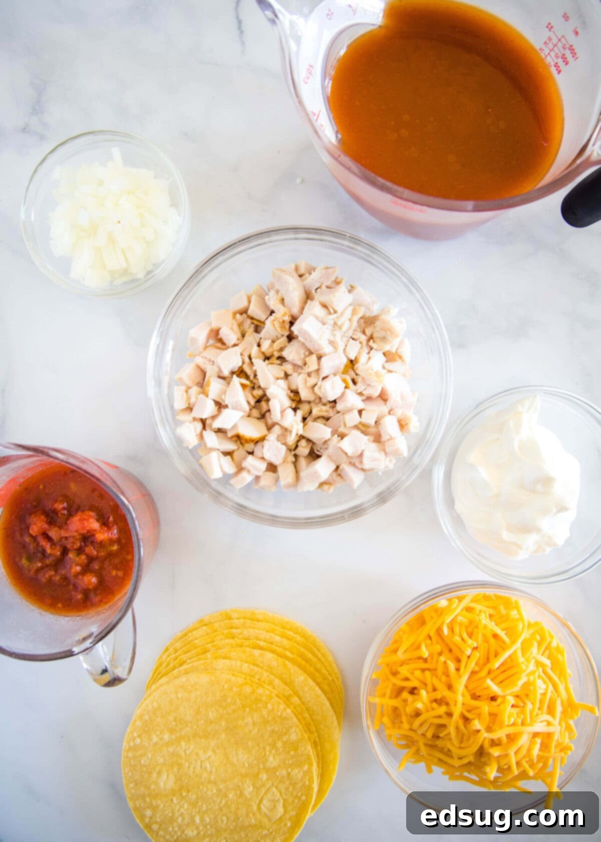 A vibrant selection of ingredients laid out on a wooden board, including shredded chicken, sour cream, cheese, onions, and corn tortillas, ready for making enchiladas.