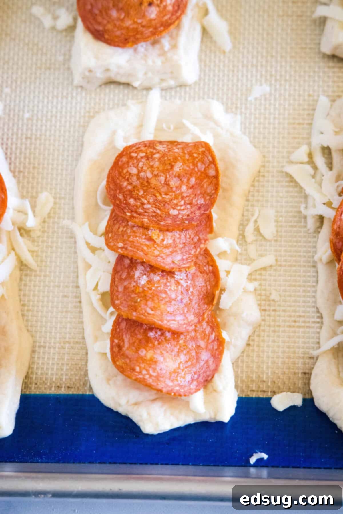 Overhead view of shredded mozzarella and pepperoni slices layered over a rolled out piece of pizza dough on a baking sheet, illustrating the filling process.