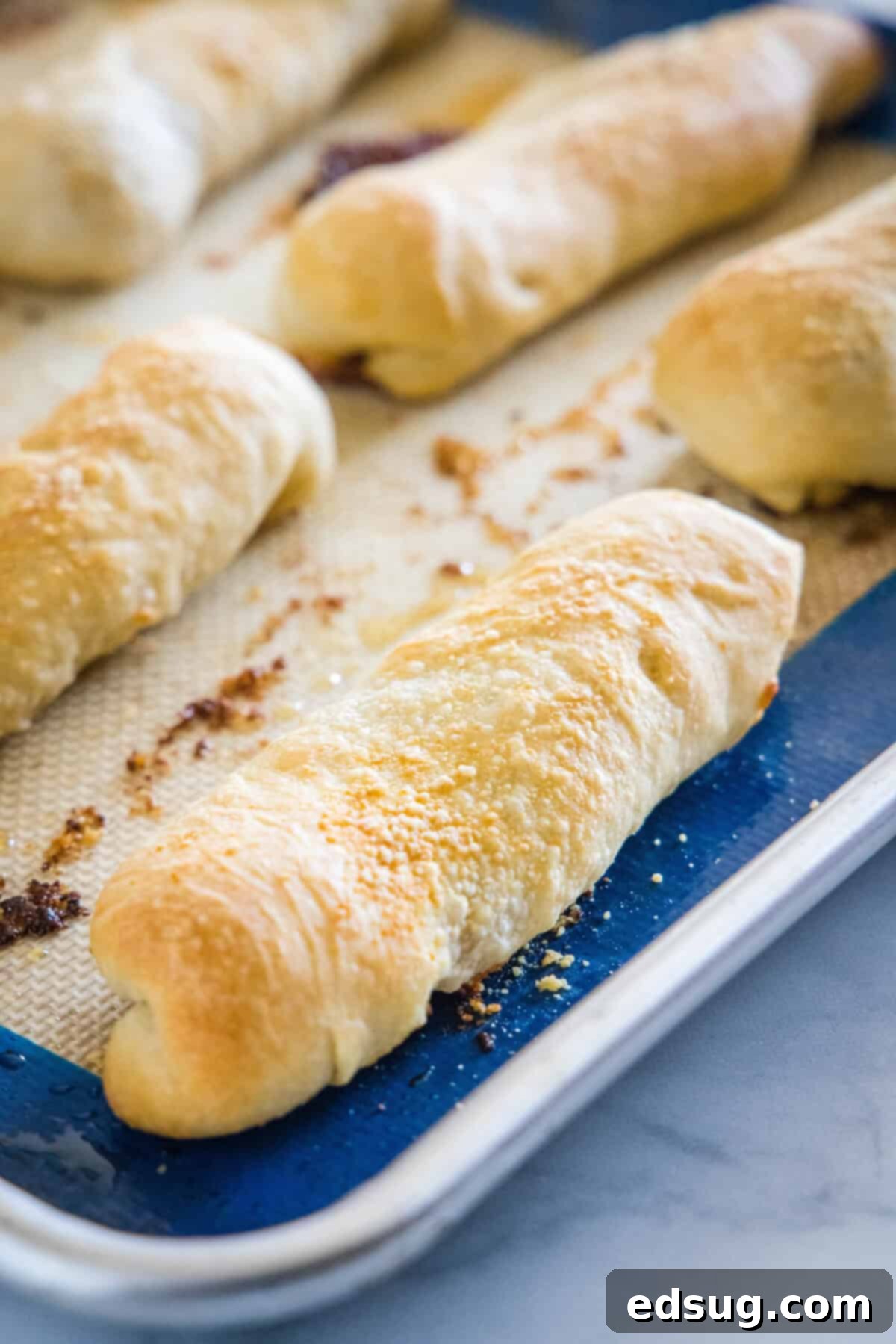 Freshly baked, golden-brown pepperoni rolls arranged on a lined baking sheet, hot from the oven.