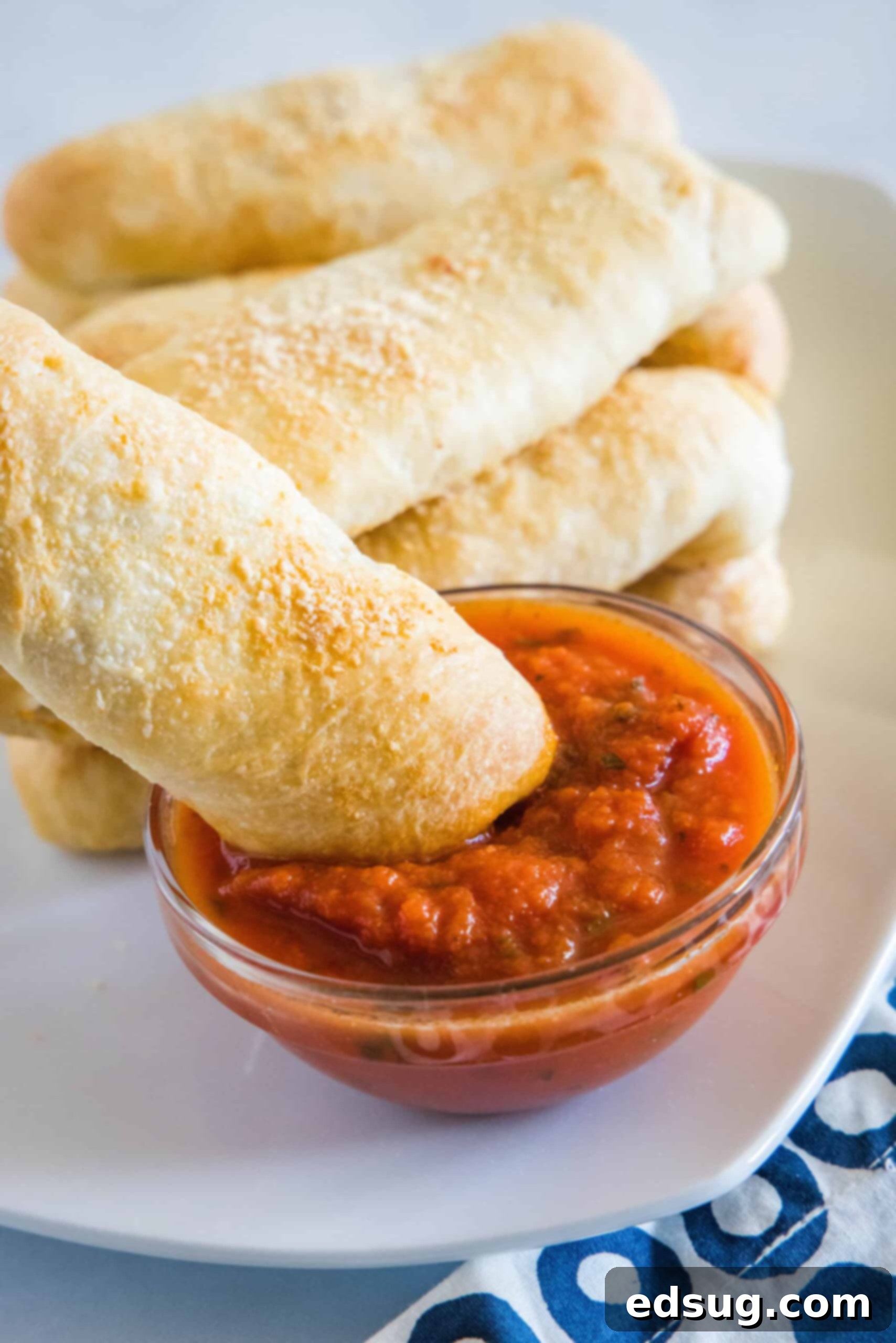 A pepperoni roll being dipped into a small bowl of marinara sauce with more rolls in the background on a plate.