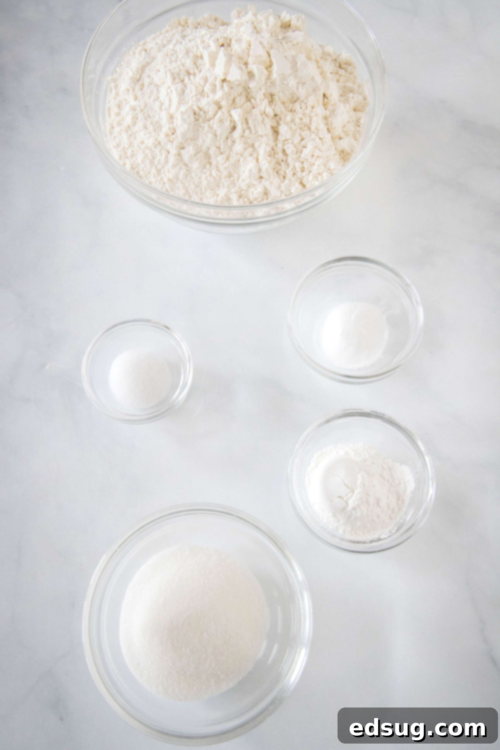 Close-up of the 5 simple ingredients for homemade pancake mix: flour, sugar, baking powder, baking soda, and salt, laid out on a clean surface.