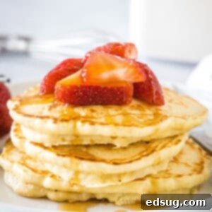 A stack of homemade pancakes topped with fresh strawberries and syrup on a white plate.