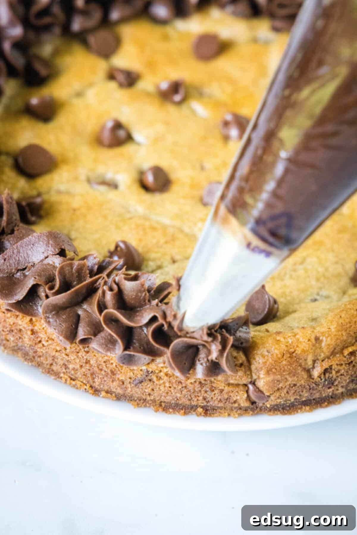 Decorating a warm cookie cake with rich chocolate frosting piped around the edges, perfect for a festive touch.