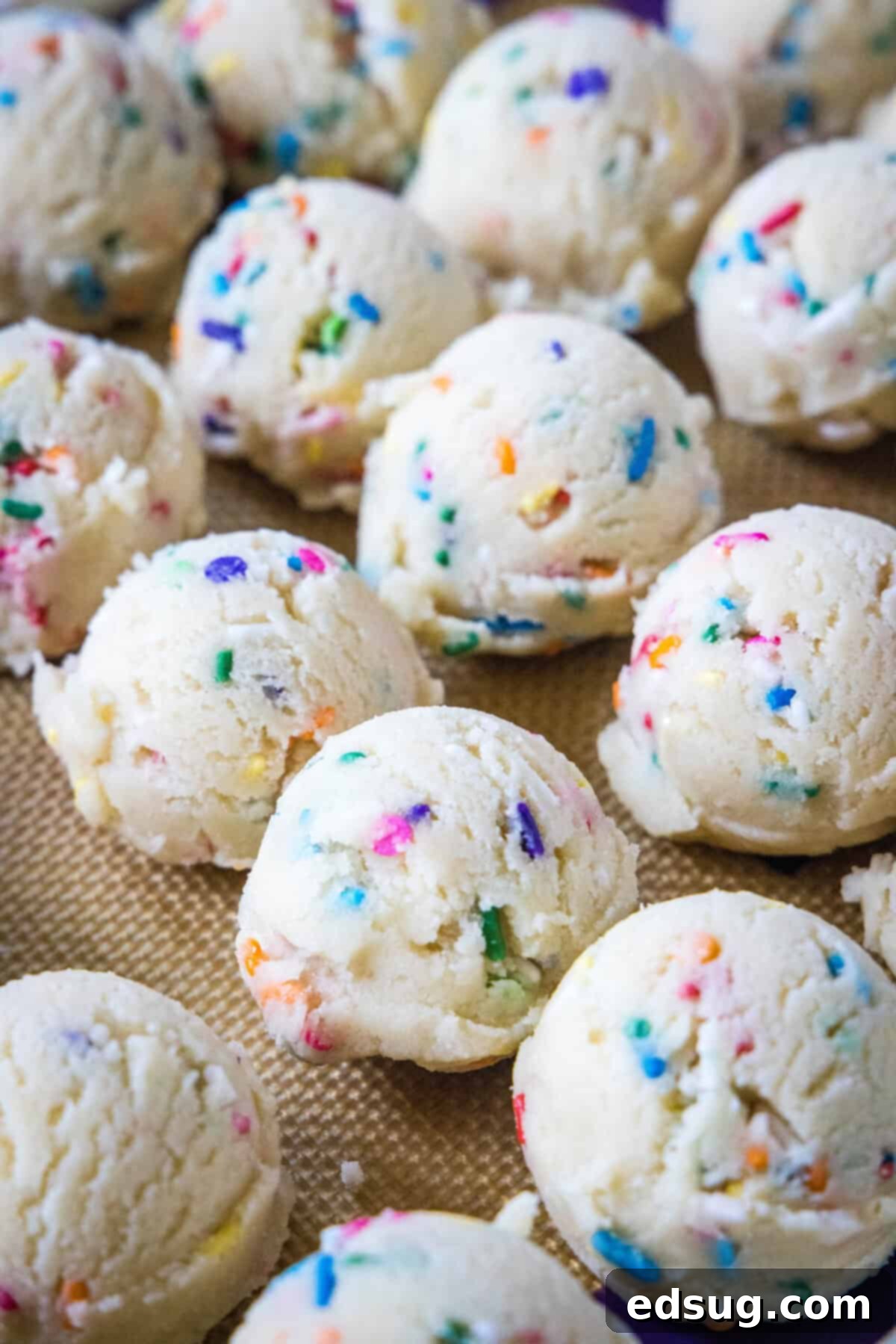 Whimsical Confetti Bites 4 Perfectly scooped balls of Funfetti cookie dough, speckled with colorful sprinkles, arranged on a baking sheet, ready for chilling.