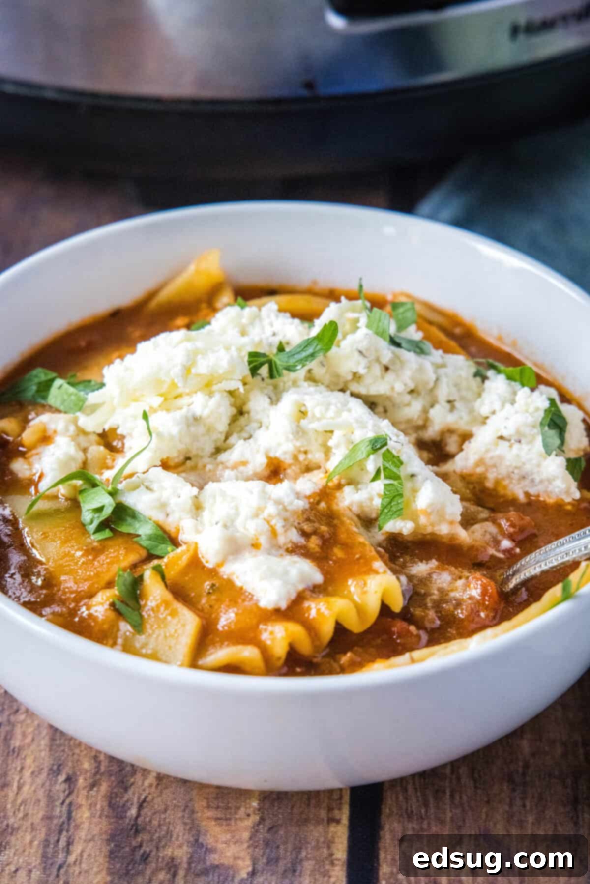 Hearty Slow Cooker Lasagna Soup 2 Hearty slow cooker lasagna soup in a white bowl, garnished with fresh herbs and creamy ricotta cheese