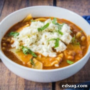 Hearty Slow Cooker Lasagna Soup 9 Close up of a serving of slow cooker lasagna soup in a white bowl with fresh basil garnish