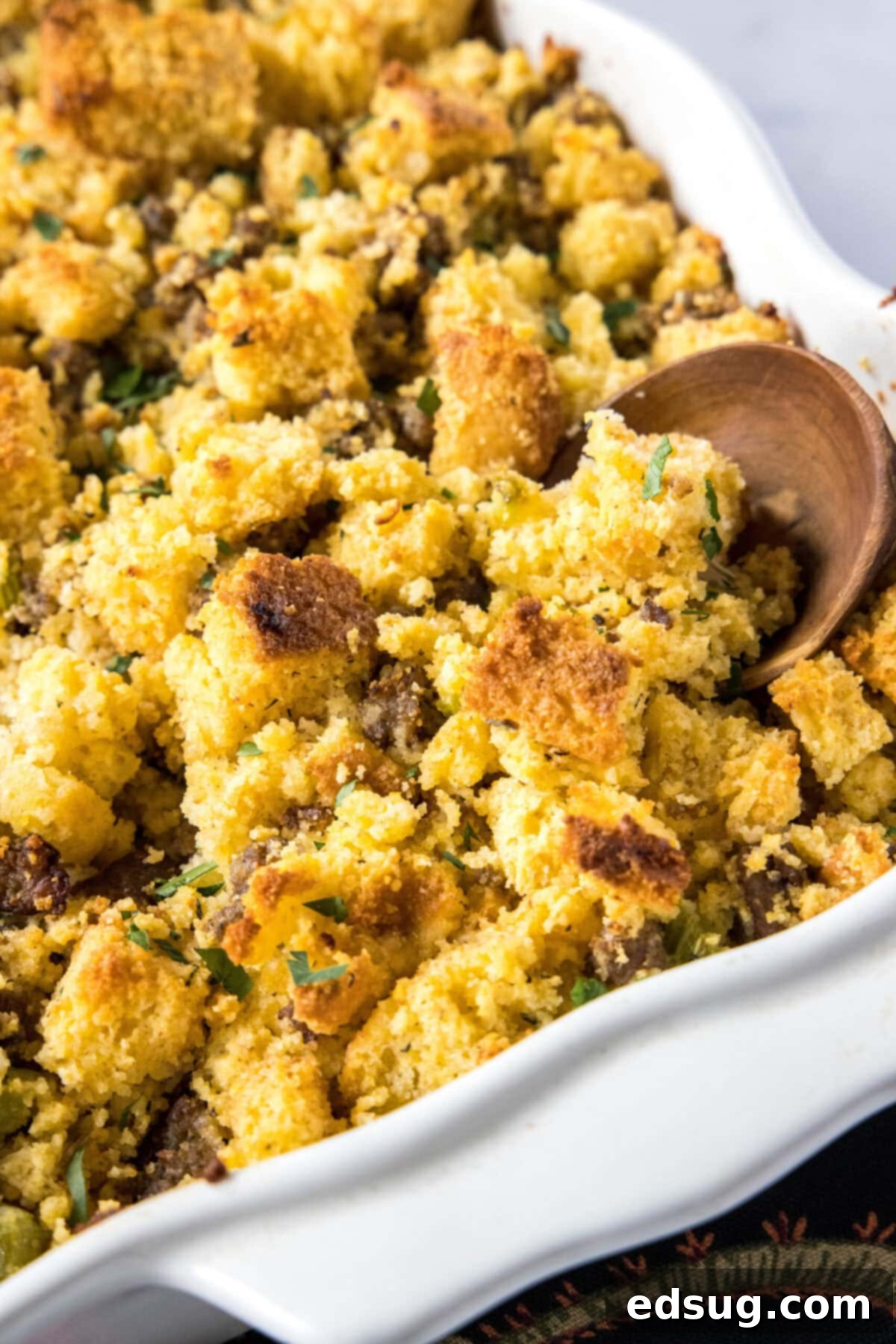 Close up of the corner of a casserole dish filled with stuffing, with a wooden spoon in it