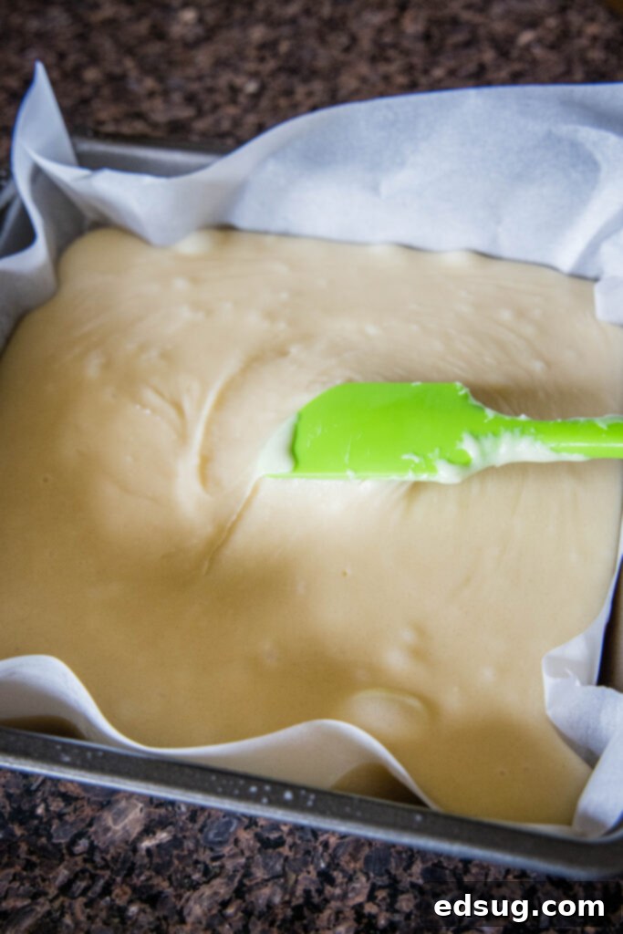 Frosted Sugar Cookie Fudge 4 Smooth, warm sugar cookie fudge being spread evenly into a parchment-lined baking pan, ready for sprinkles.