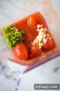Tomatoes, jalapeño, and garlic cloves being added to a blender, ready to be pureed for the chilaquiles sauce base.