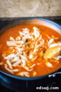 Shredded cooked chicken being added to and stirred into the simmering spicy tomato sauce in a skillet, ensuring it is well coated and heated.