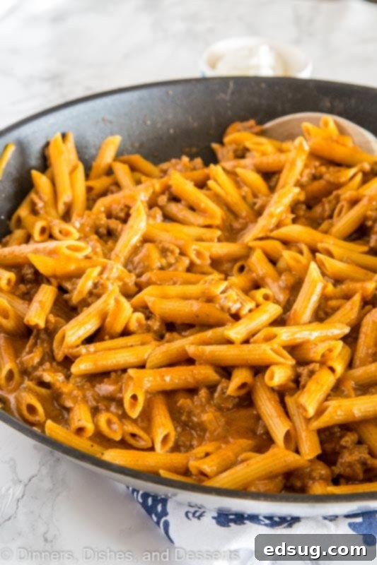 A generous serving of hot Cheesy Skillet Chili Mac in a white ceramic bowl, garnished with fresh chopped green onions and a dollop of sour cream, ready to be enjoyed.