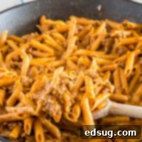 Close up of penne pasta with ground beef, spices, and cheese in a skillet, representing Cheesy Skillet Chili Mac.