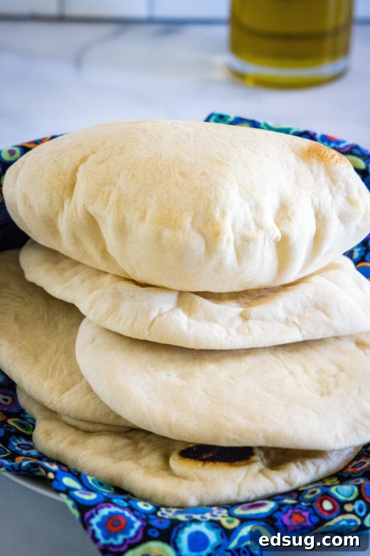 Crafting Perfect Pita 13 A close-up shot of fluffy homemade pita breads stacked on a blue cloth, ready for serving.