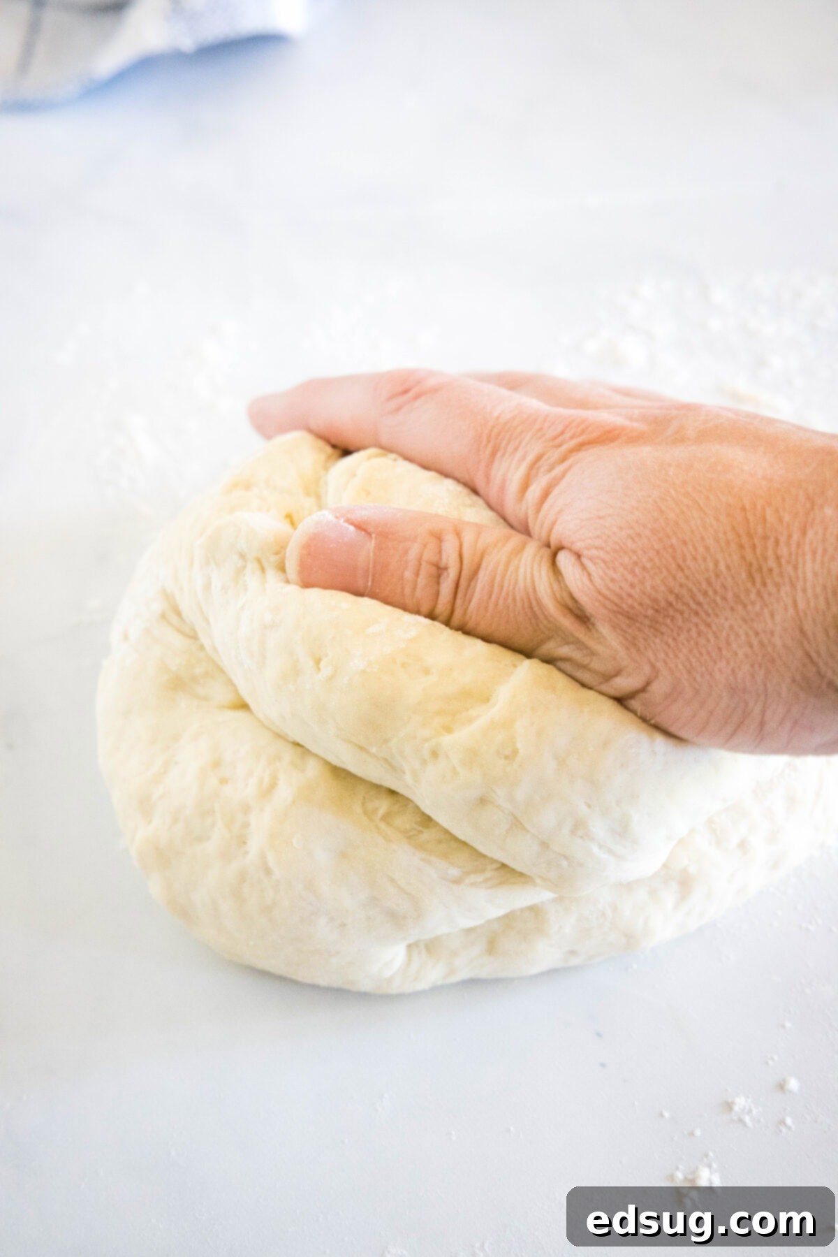 Crafting Perfect Pita 6 A hand gently kneading soft pita dough on a lightly floured white surface.