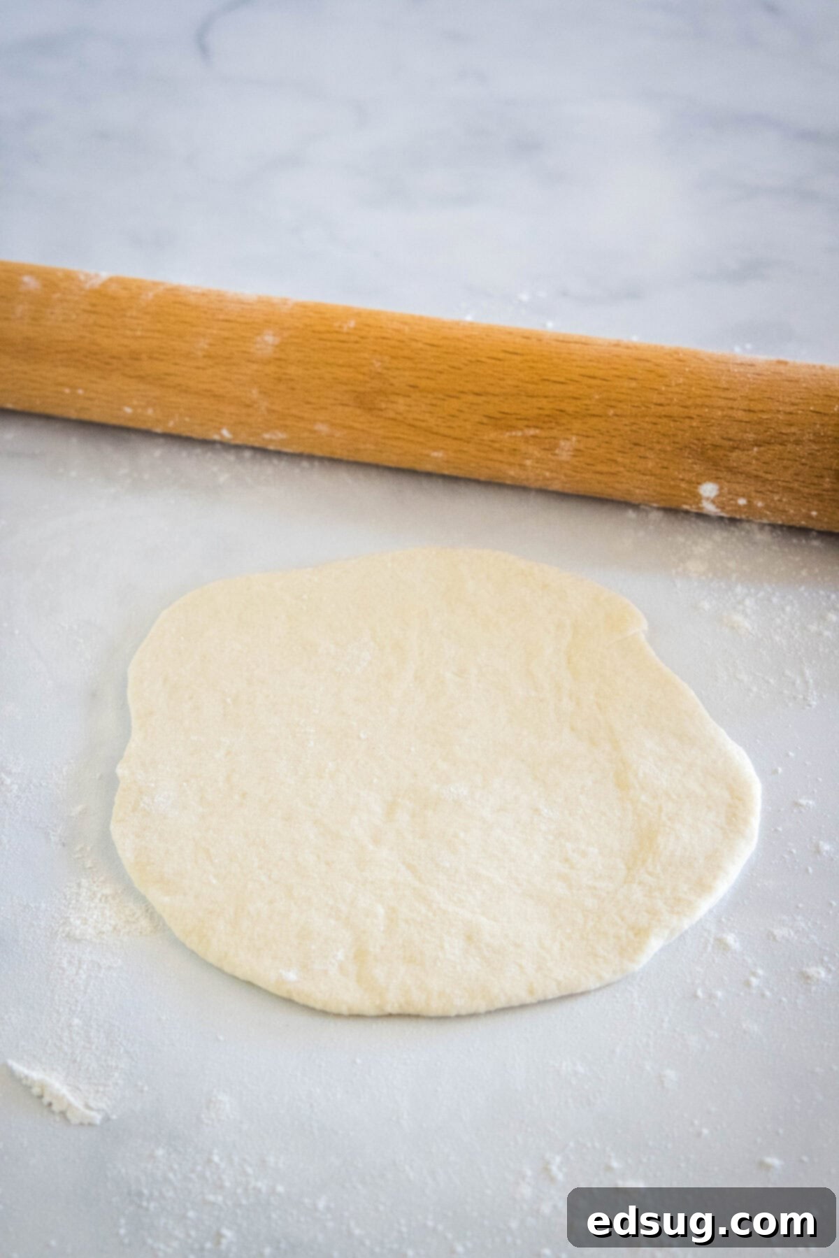 Crafting Perfect Pita 9 A piece of pita bread dough expertly rolled out into a flat, uniform circle on a floured surface.