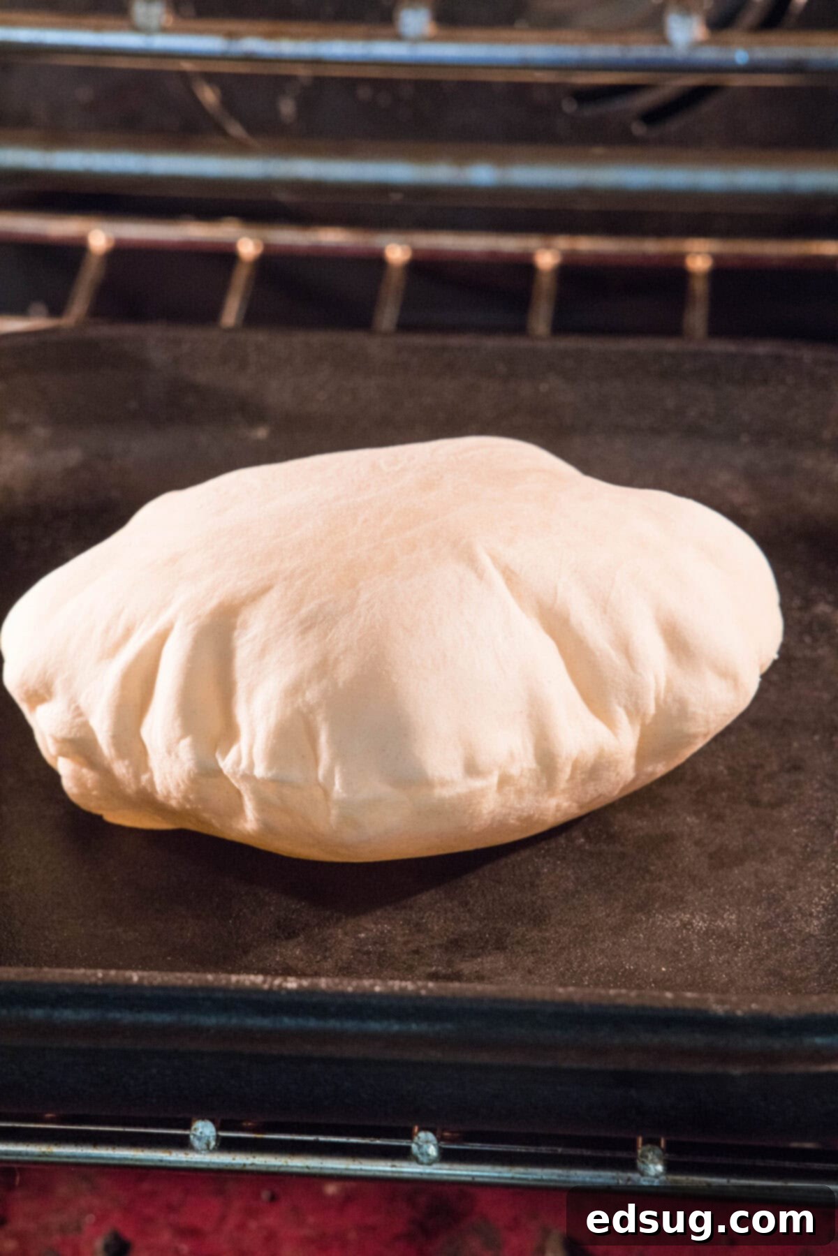 Crafting Perfect Pita 10 A pita bread rapidly puffing up into a balloon-like shape on a hot pan inside the oven.