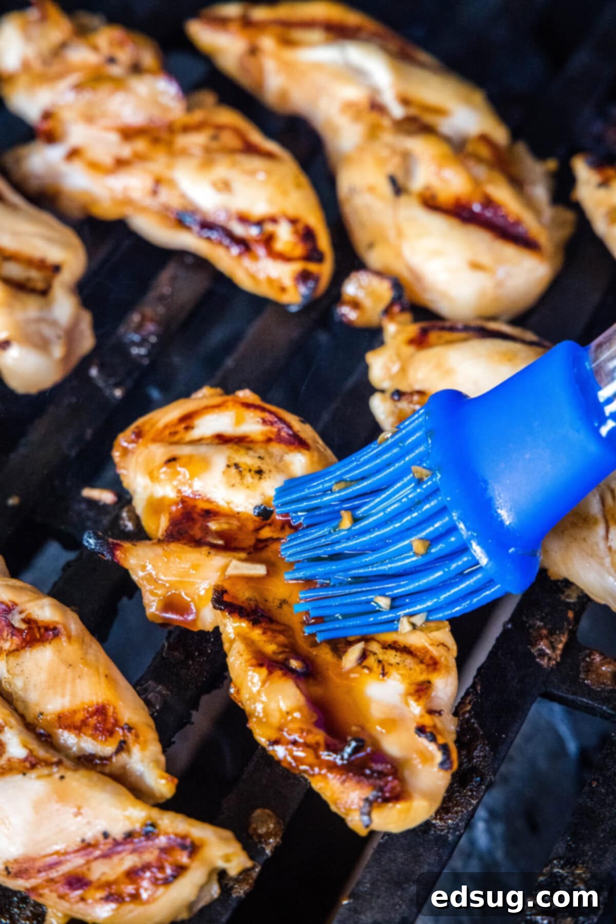 Sweet & Sticky Grilled Teriyaki Chicken 5 A vibrant red rubber basting brush applies sticky teriyaki sauce to chicken pieces cooking on a hot grill, creating a beautiful glaze.