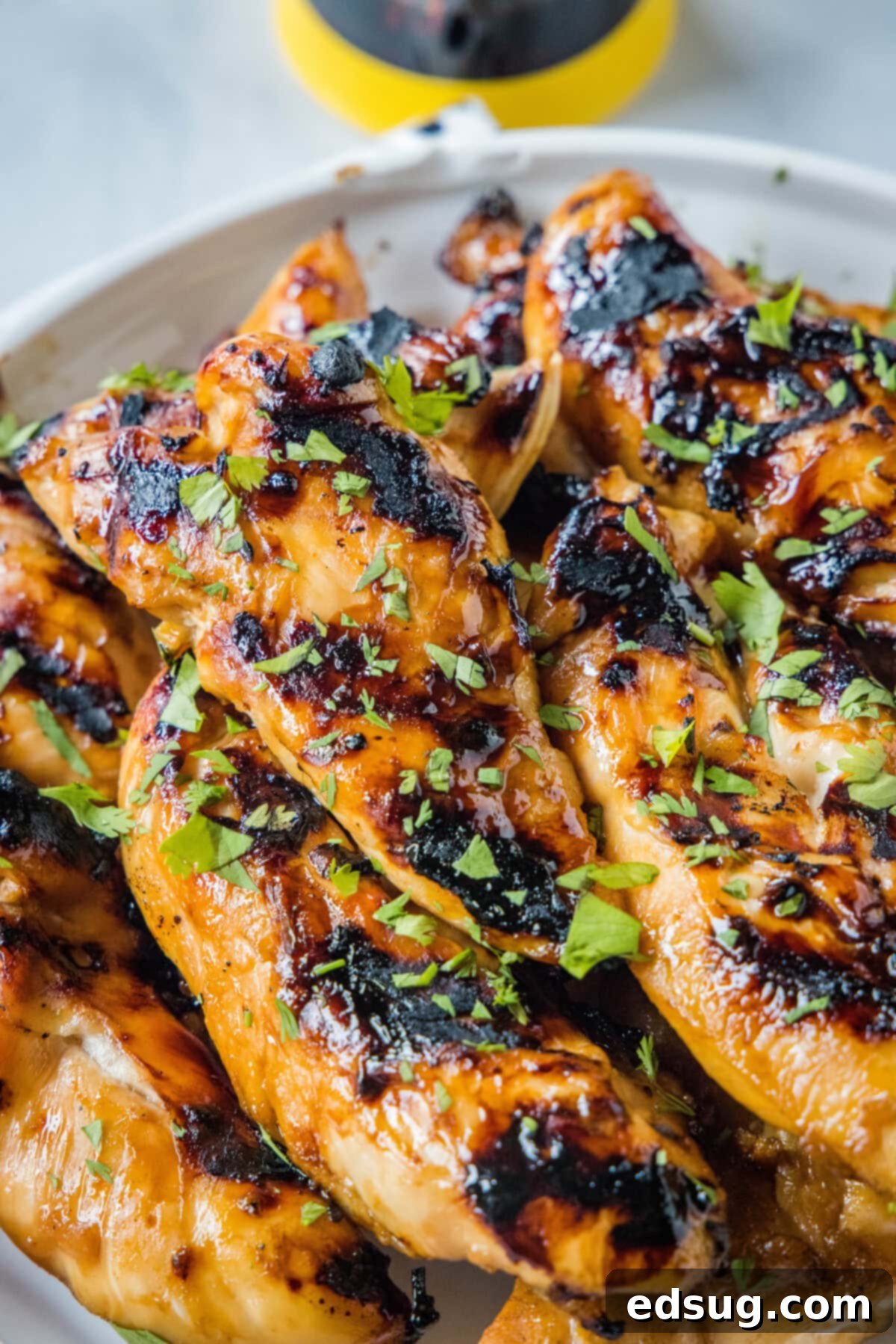 Sweet & Sticky Grilled Teriyaki Chicken 6 A close-up view of perfectly grilled teriyaki chicken, glistening with sauce and garnished with fresh green onions, piled on a white serving platter.