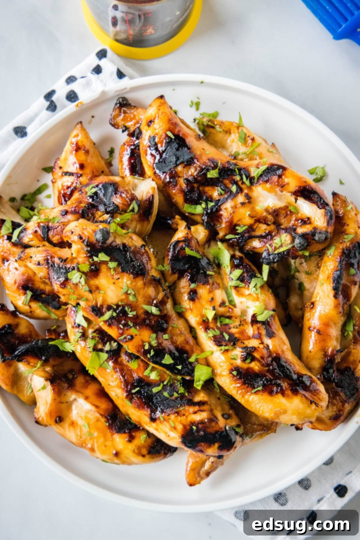 Sweet & Sticky Grilled Teriyaki Chicken 7 An overhead shot of grilled teriyaki chicken, garnished with sesame seeds and chopped green onions, arranged artfully on a white platter.