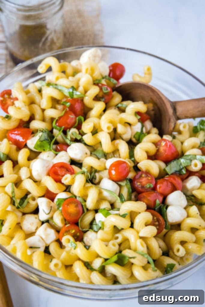 caprese pasta salad in a bowl with a wood serving spoon