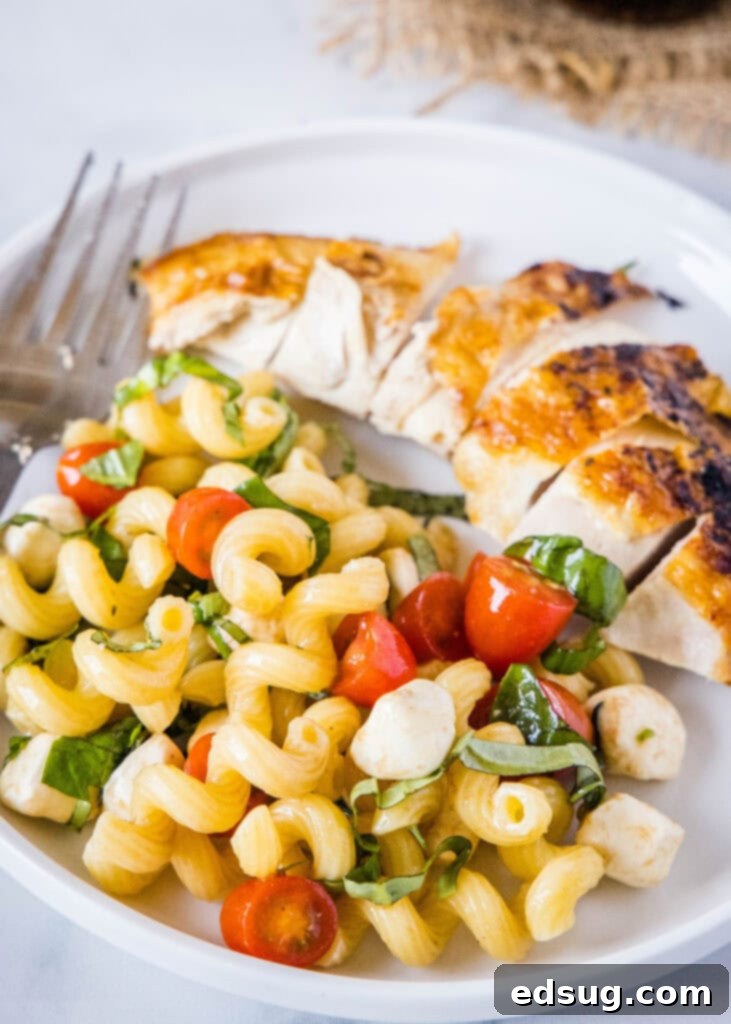 caprese pasta salad on a plate with a piece of chicken