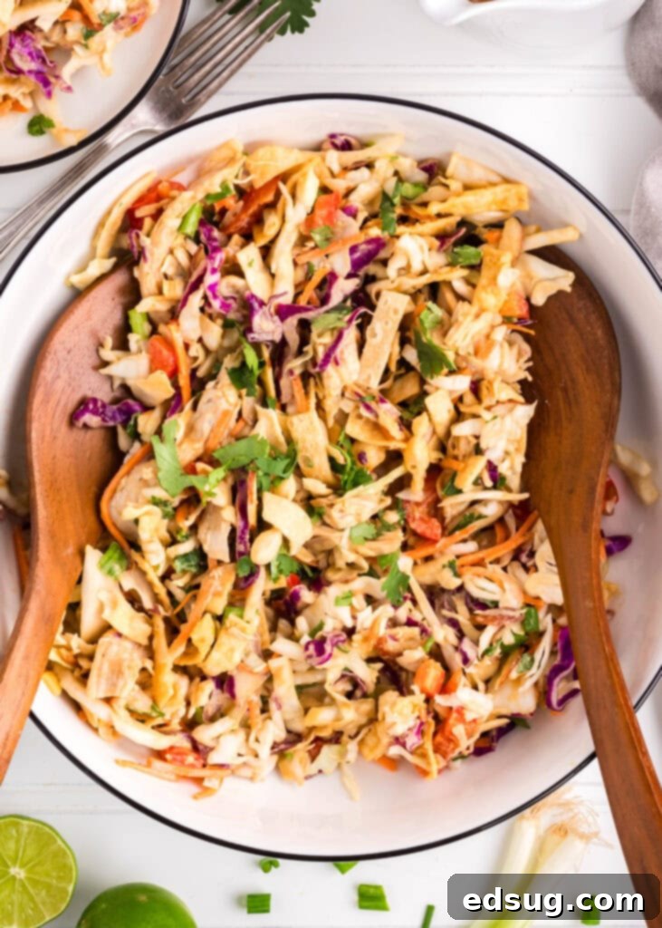 a serving bowl filled with Thai chicken salad, with wooden spoons ready to serve