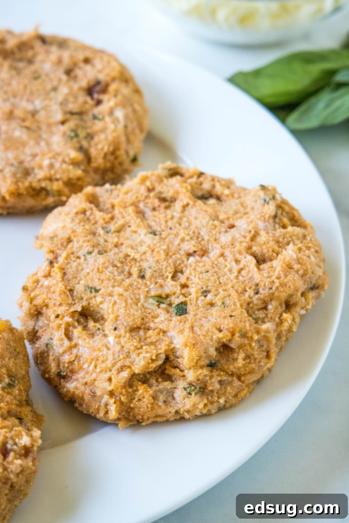 Chicken Parm Burgers 4 Raw chicken parmesan burger patties mixed with ingredients on a ceramic plate, ready for cooking.
