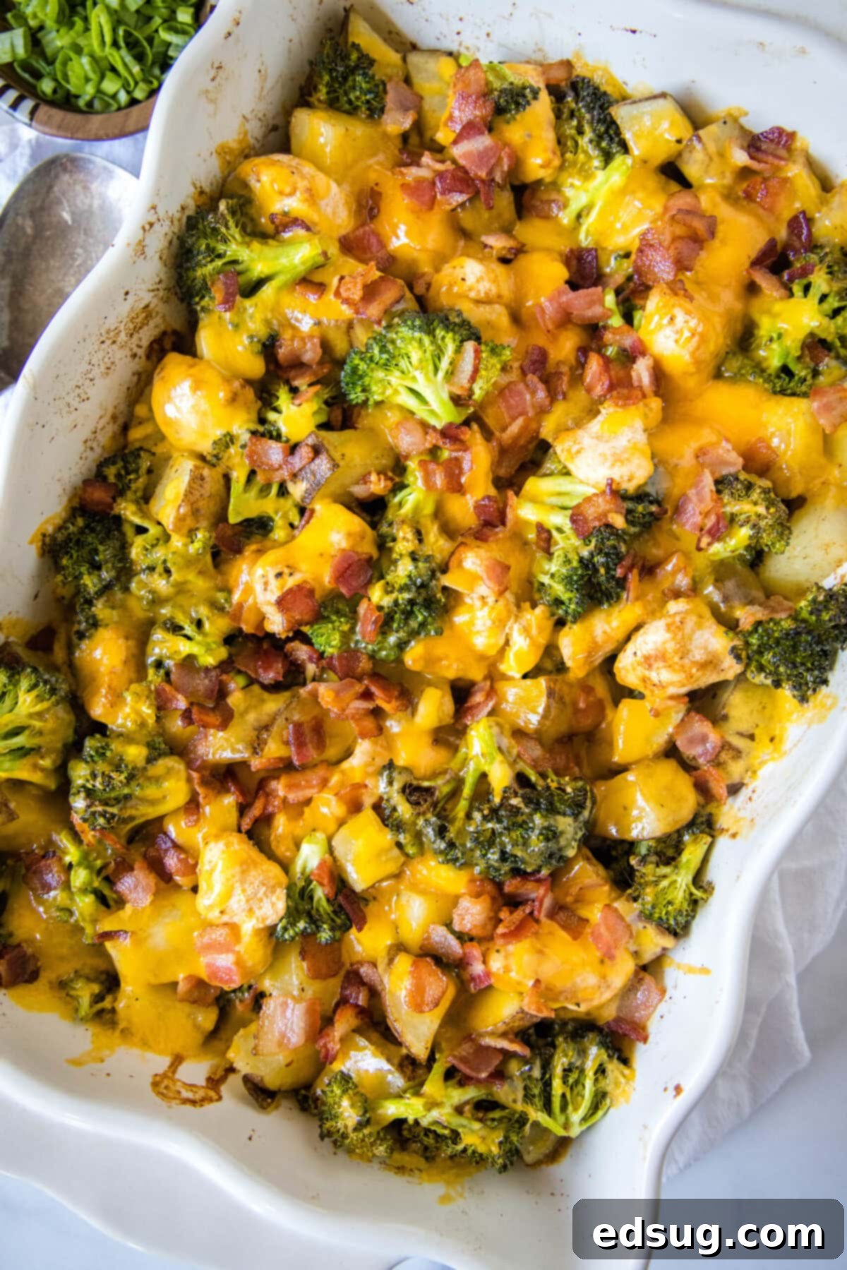 Overhead view of a rectangular casserole dish brimming with potatoes, chicken, and green broccoli florets, generously topped with golden melted cheese and crispy bacon pieces.