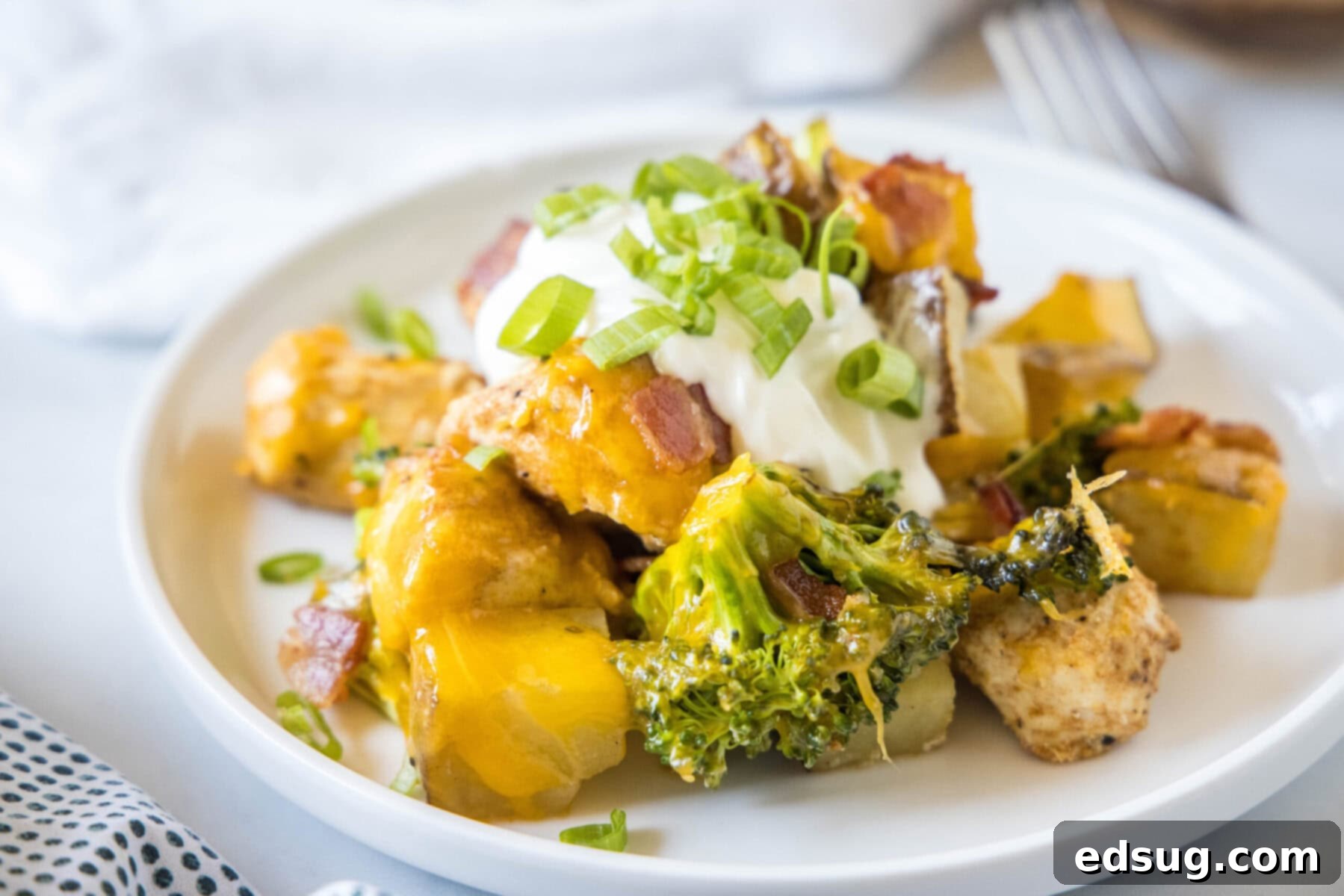 A perfectly portioned serving of the Loaded Chicken Potato Casserole on a round white plate, beautifully garnished with a generous dollop of sour cream and vibrant green onions, ready to be enjoyed.