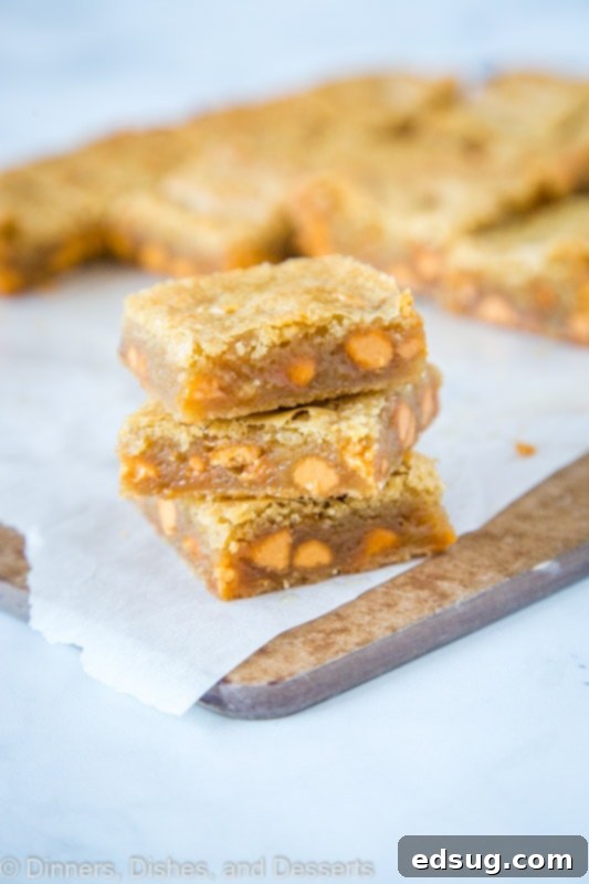 Golden Butterscotch Blondies 4 Stacked Butterscotch Blondies on a cutting board, showcasing their rich, buttery texture and generous butterscotch chips throughout.