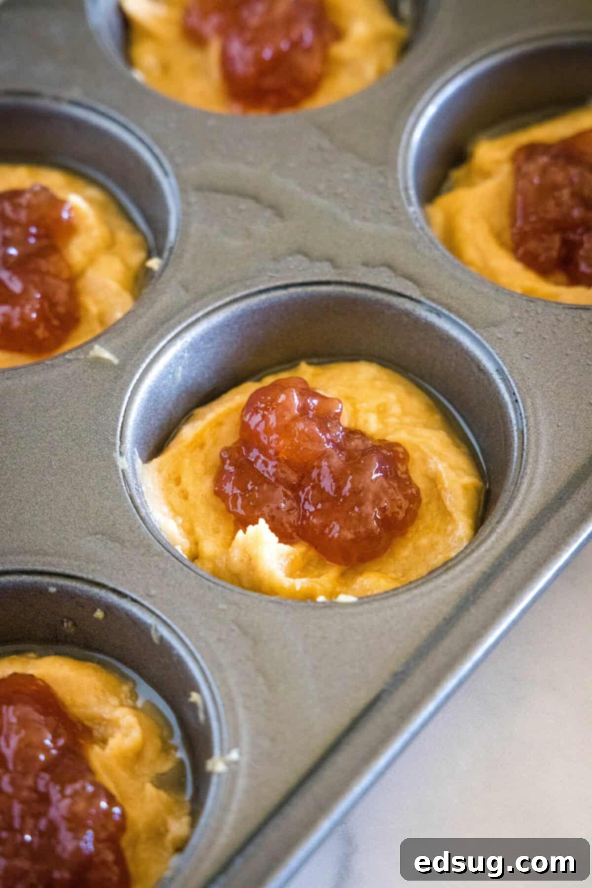 Peanut Butter and Jelly Swirl Muffins 4 Jelly being spooned into the middle of peanut butter muffin batter in a muffin tin