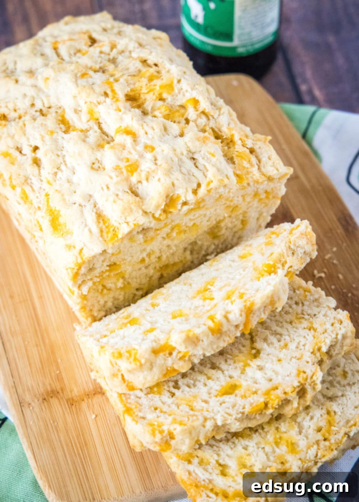 Overhead view of a golden brown loaf of cheddar beer bread with three inviting slices cut off, revealing its moist crumb and pockets of melted cheese.
