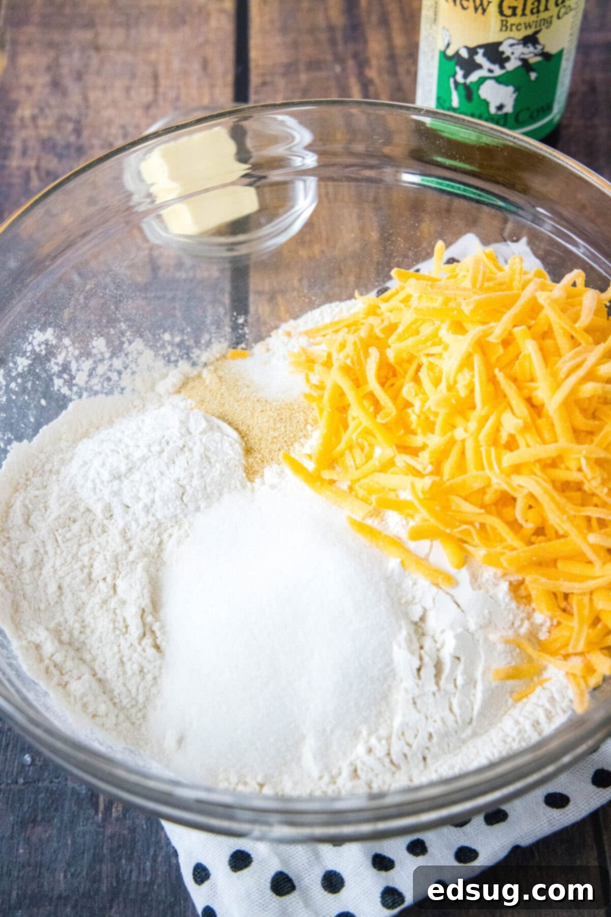 A large mixing bowl filled with all the pre-measured dry ingredients for cheddar beer bread: flour, shredded cheddar cheese, salt, sugar, baking powder, and garlic powder, perfectly mixed and ready for the wet ingredients.