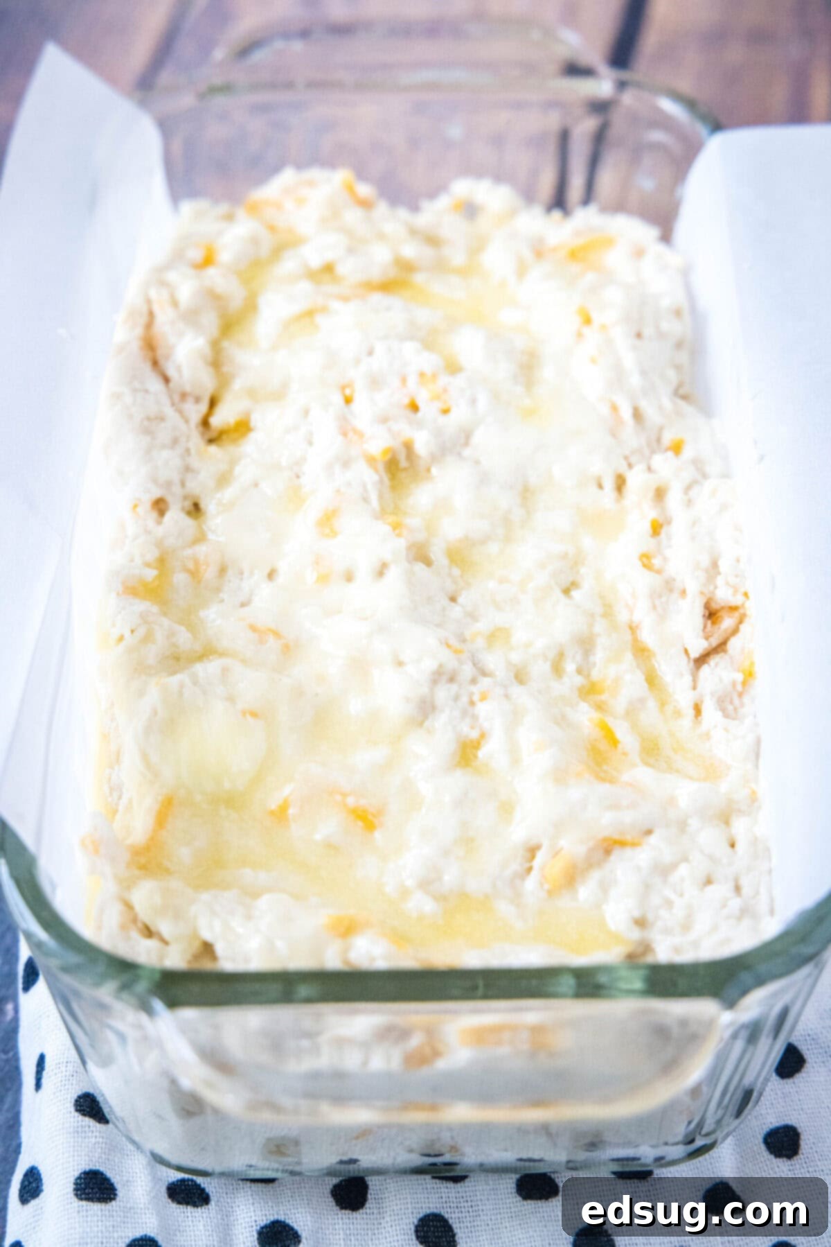 A loaf pan meticulously filled with the prepared cheddar beer bread batter, glistening with melted butter brushed over its surface, now perfectly ready to be placed into the oven for baking.