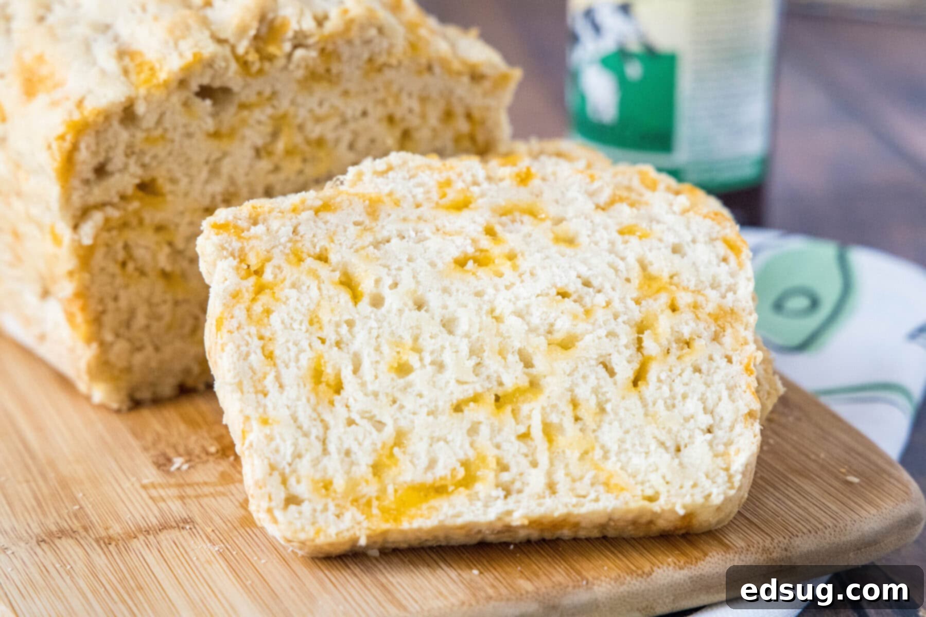 Close-up of a warm, inviting slice of cheddar beer bread, golden and perfectly baked, leaning against the main loaf, ready to be picked up and savored.