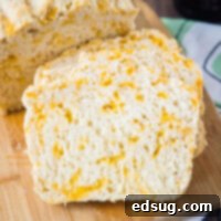 Close up of two golden slices of cheddar beer bread leaning against a rustic loaf of bread, highlighting the perfect texture and inviting cheesy interior.