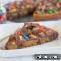 Ultimate Candy Bar Cookie Pizza 2 Delicious Candy Bar Cookie Pizza on a white plate, topped with colorful candies and melted chocolate.
