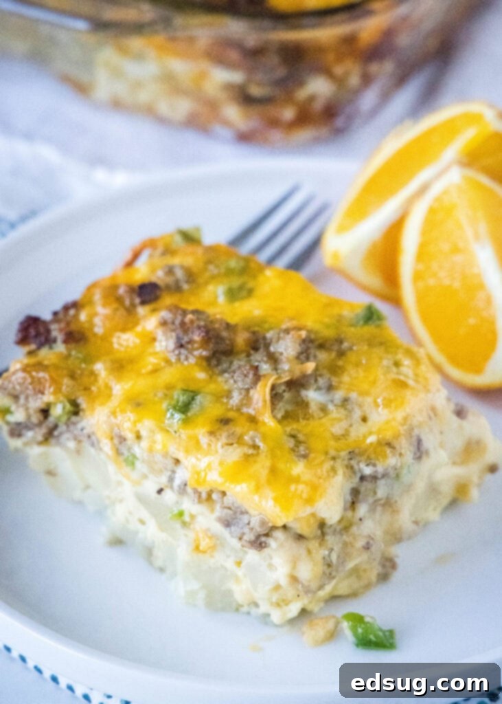 A white plate with a slice of baked sausage egg casserole and fresh orange slices