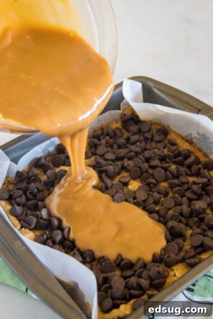 Chewy Caramel Bars 4 Melted caramel being poured over a layer of chocolate chips and a baked cookie base in a square pan