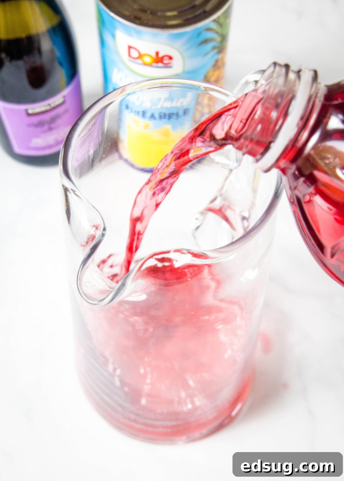 Pouring cranberry juice into a large pitcher, beginning the preparation of the festive punch.